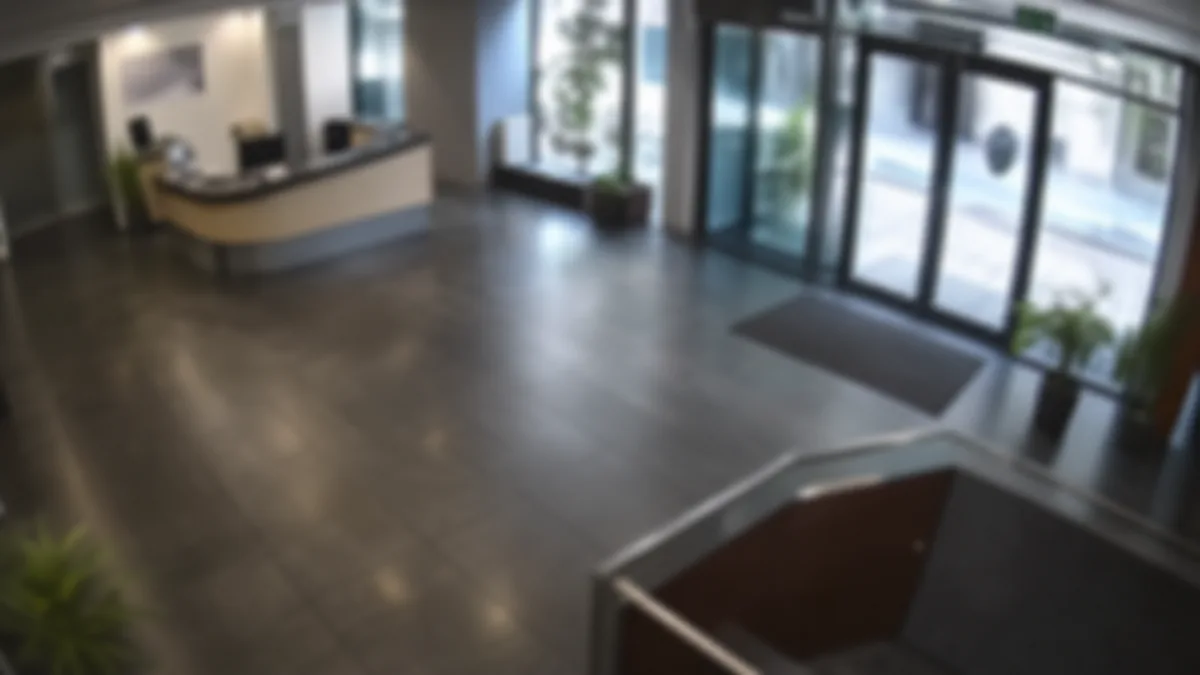 Blur degradation in an office lobby CCTV view, with the entrance and reception area soft and hard to inspect.