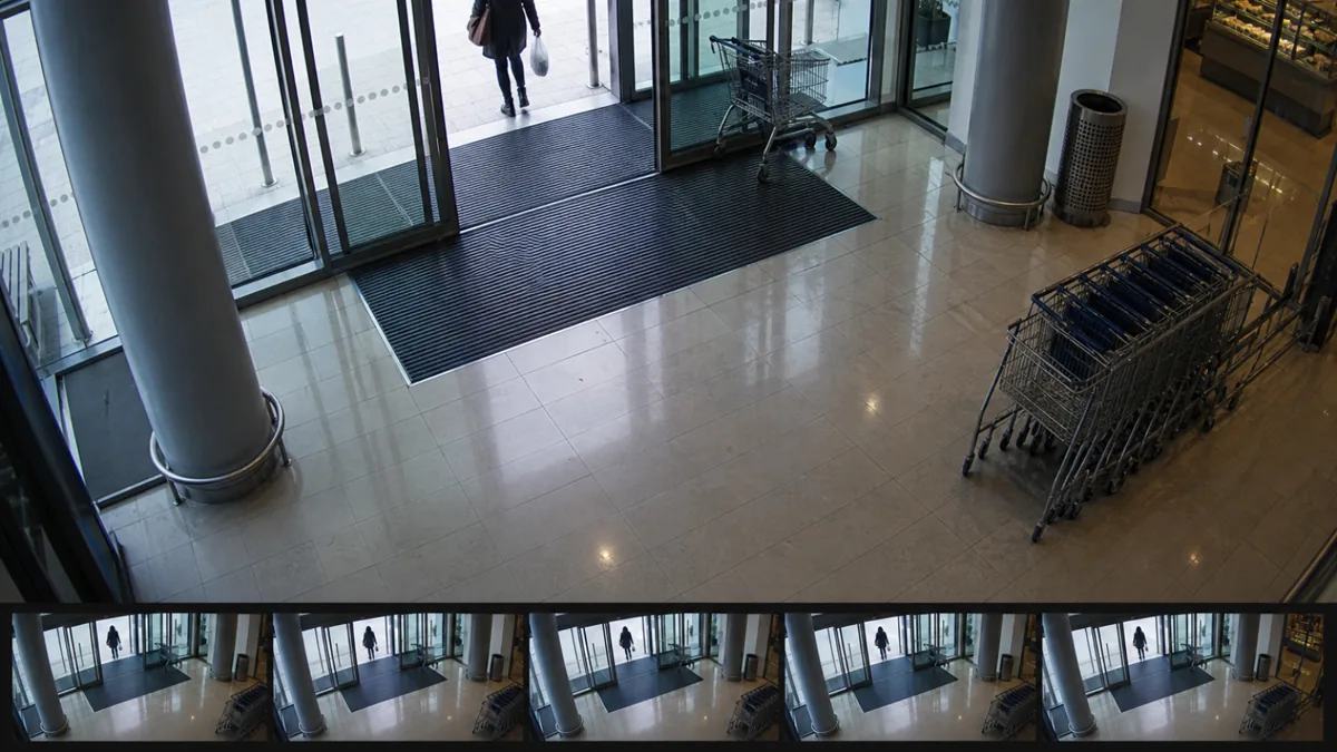 Camera freeze degradation in a shopping centre entrance CCTV view with repeated identical entrance frames.