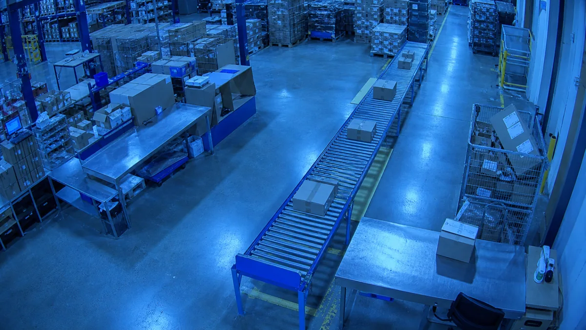 Colour cast degradation in a warehouse packing station CCTV view with an abnormal blue tint.
