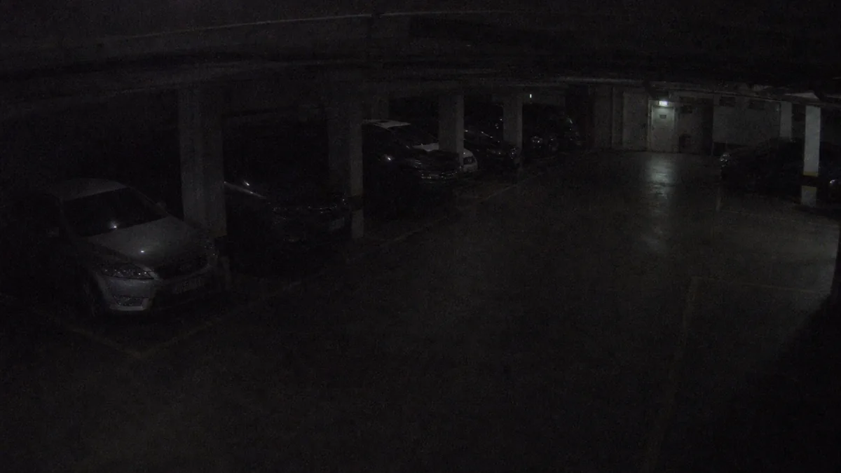 Darkness degradation in an underground parking CCTV view, where cars and pillars are barely visible.