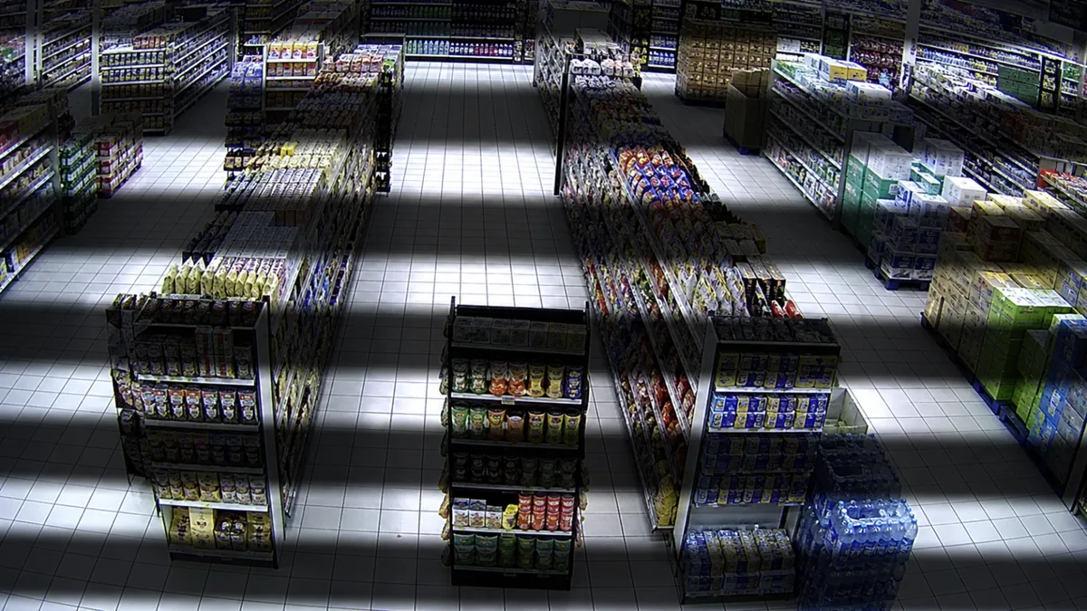 Flicker degradation in a retail aisle CCTV view with alternating bright and dark exposure bands.