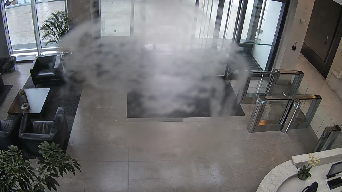 Occlusion degradation in an office lobby CCTV view, with a cloudy smear hiding the central entrance area.