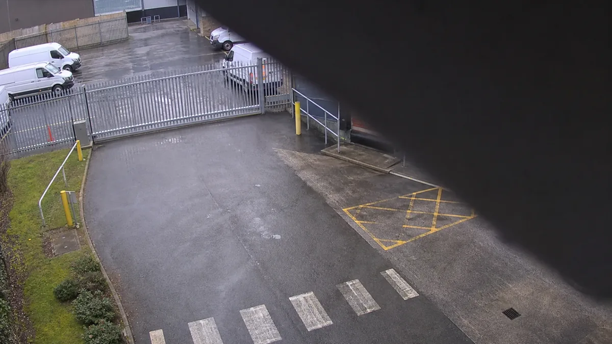 Occlusion degradation in an industrial yard CCTV view, with debris blocking the upper edge of the scene.