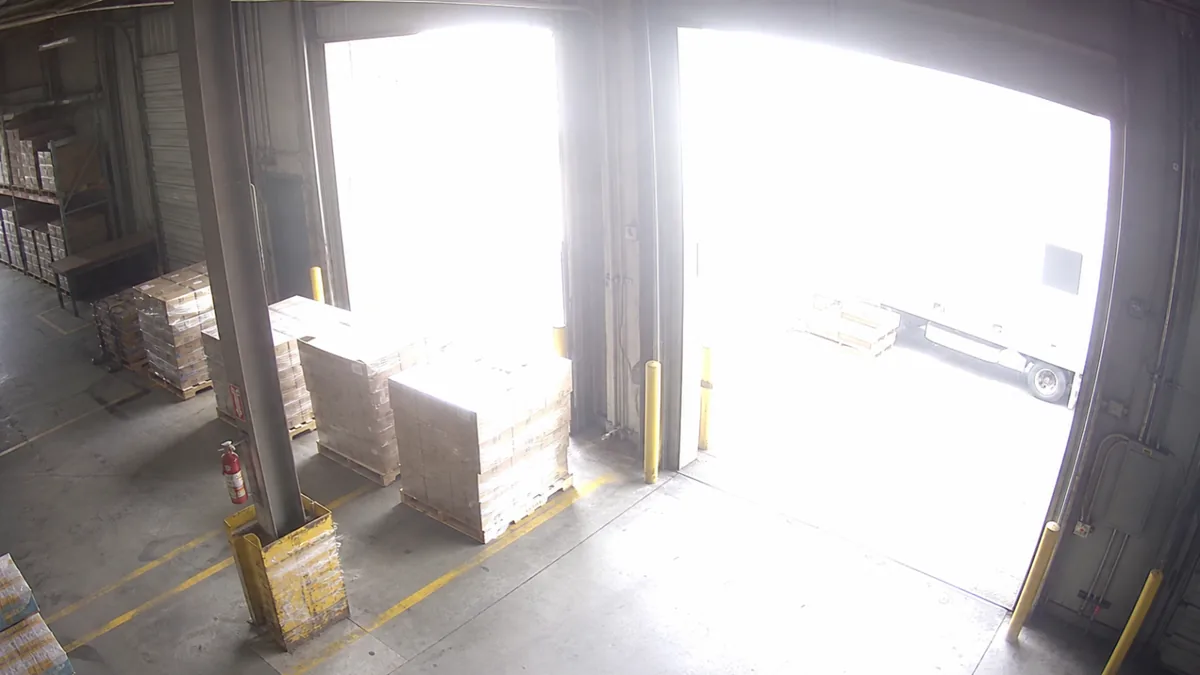 Overexposure degradation in a loading dock CCTV view, with daylight blowing out the dock doorway.