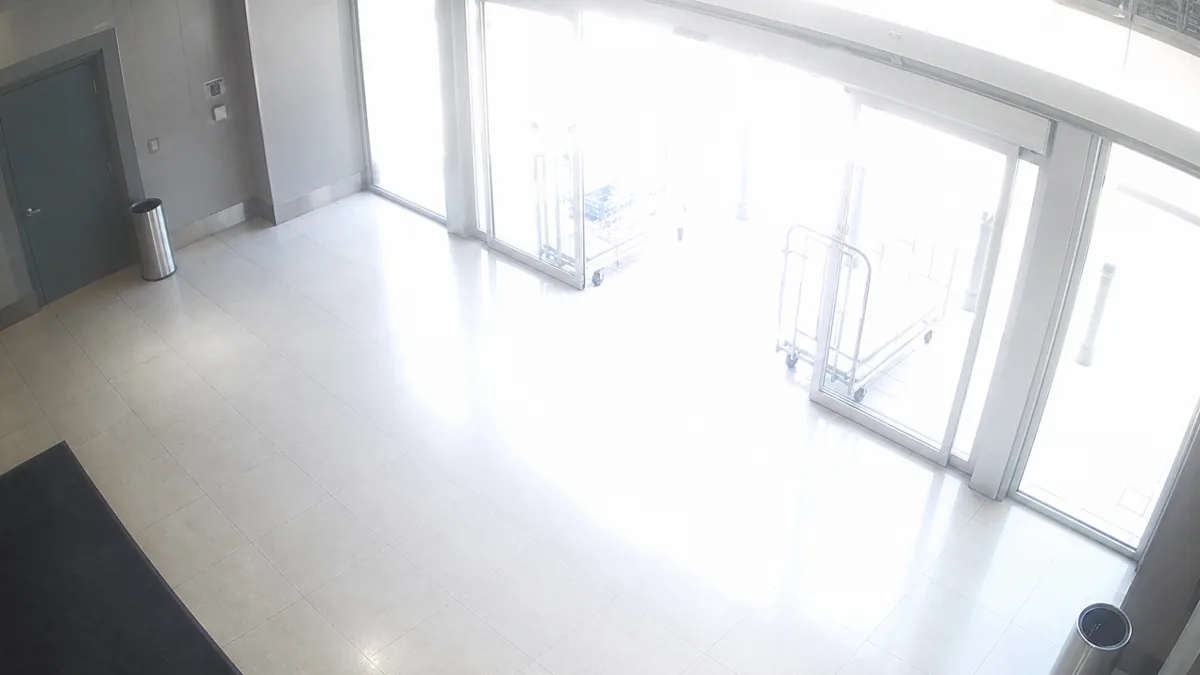 Overexposure degradation in a shopping centre entrance CCTV view, where the doors and carts are washed out.