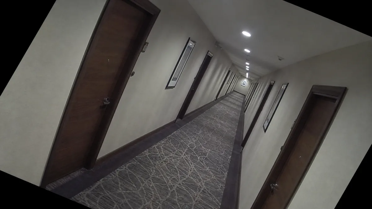 Tilt degradation in a hotel corridor CCTV view, with doors and ceiling lights visibly slanted.