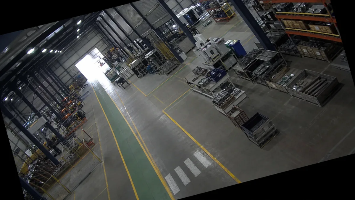 Tilt degradation in a manufacturing floor CCTV view, with safety lane lines rotated across the frame.
